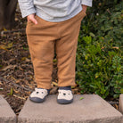 Child wearing brown pants and white shoes with bear design outdoors