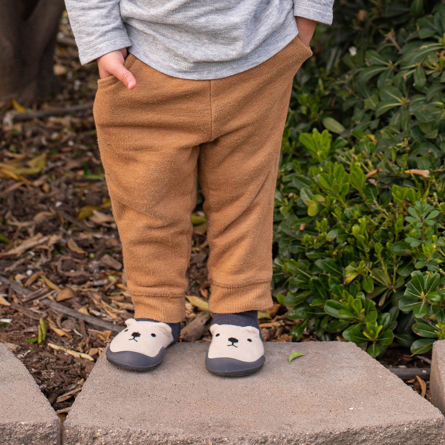Child wearing brown pants and white shoes with bear design outdoors