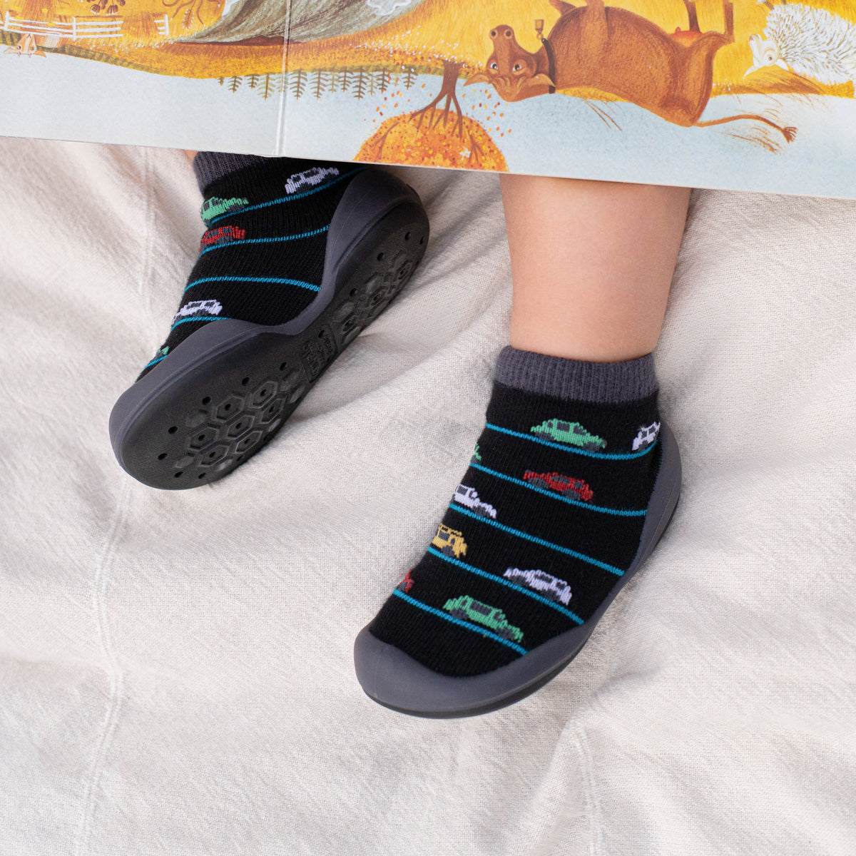 Child wearing socks with a car pattern and gray sock shoes while reading a book.