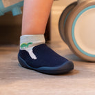 A baby's foot wearing a navy blue sock-shoe with a dinosaur on the sock.
