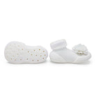 A pair of white baby shoes, one with a flower.

