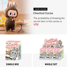 Close-up studio shot of the "Chestnut Cocoa" secret edition figure from the "Exciting Macarons" toy series. The figure, with large, expressive eyes, fluffy brown fur, and bunny ears, holds a pastry next to a miniature table with a dessert and a drink. Below are images of the product's single box and a whole set of multiple boxes.