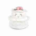 Plush toy resembling a two-tiered cake with a smiling face and pink flower on top against a white background