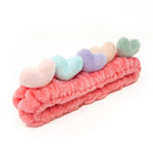 Pink plush headband with five pastel hearts.
