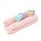 Pink, plush headband with multi-colored heart embellishments.