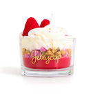 Candle in a glass container with red jelly, white cream, and raspberries on a white background