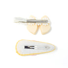 Two hair clips, one light yellow bow with a white and silver clip, and one pastel fabric clip with a silver clip. Both clips are against a white background.