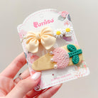 A set of three hair clips: a yellow bow, two daisy flowers, and a pink and green embroidered leaf shape with pearls, all displayed on a floral patterned card.