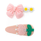 Two hair clips: one with a pink bow and white daisies; another with a pink knit strawberry and green leaves, embellished with pearls.