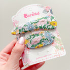 Two floral print hair clips on a decorative card held in a hand.
