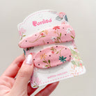 Two pink fabric hair clips with floral pattern on a floral-themed display card, held in a hand.