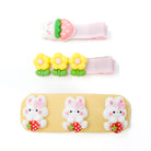 A set of three children's hair accessories featuring cute designs: a strawberry-bunny clip, a three-flower clip, and a bunny-strawberry hair tie.