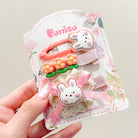 Hand holding a card of children's hair accessories featuring bunny and flower designs in pink and white.
