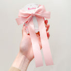 A hand holds a pink bow hair clip.