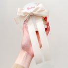 Hand holding hair accessory with ivory bow and floral pattern.
