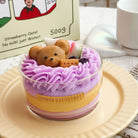 Candle with a teddy bear design on a plate, with a cup and package in the background.