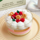 Scented candle with whipped cream, berries, and waffle pieces on a light surface.