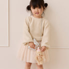 Plush tan bunny keychain with pink hat and bow, attached to silver chain, held by child in beige sweater and tulle skirt, lifestyle front view