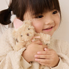 Soft beige plush bunny keychain with pink party hat and ribbon, held by child in cozy knit sweater, lifestyle close-up.