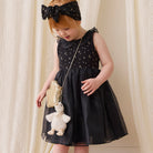 White plush duck keychain with beige bow, attached to gold crossbody bag, worn by child in black floral dress and headband, lifestyle side view