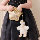 Soft white plush duck keychain with beige bow, by Snuggle Bunnies, attached to gold star-shaped pouch, worn by child in black floral dress.