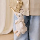 White plush duck keychain with beige bow by Snuggle Bunnies, hanging from gold bag, side view, soft texture, small size