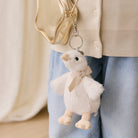 White plush duck keychain with beige bow, by Snuggle Bunnies, hanging from gold zipper bag, side view, soft texture, small size