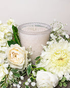 White candle with decorative pearls surrounded by white flowers on a light background